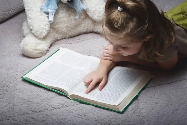 Mooi klein meisje lees boek met favoriete beer — Stockfoto