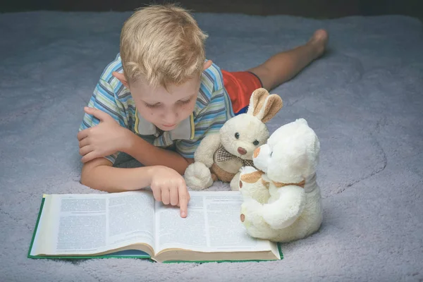 Kleine jongen lezen boek met zijn favoriete speelgoed — Stockfoto