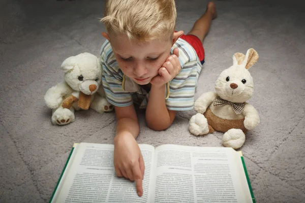 Kleine jongen lezen boek met zijn favoriete speelgoed — Stockfoto