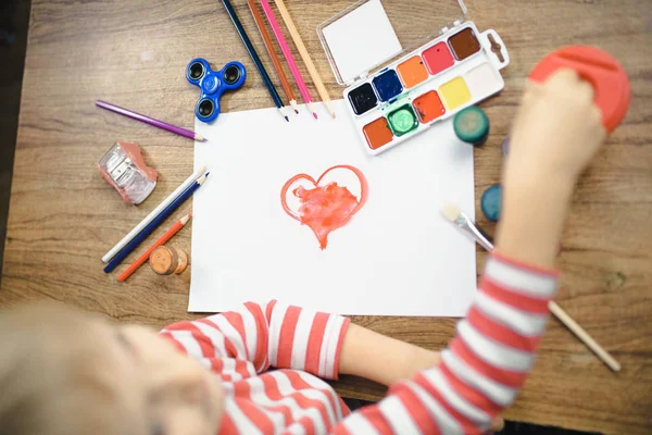 Şirin çocuk kağıt üzerinde kırmızı bir kalp boyalar