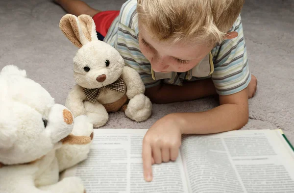 Kleine jongen lezen boek met zijn favoriete speelgoed — Stockfoto