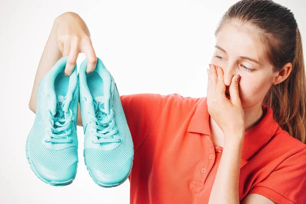 Kız pis kokulu ayakkabılarını tutuyor ve burnunu kapatıyor.