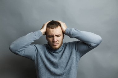 Guy in a blue sweater is holding his head