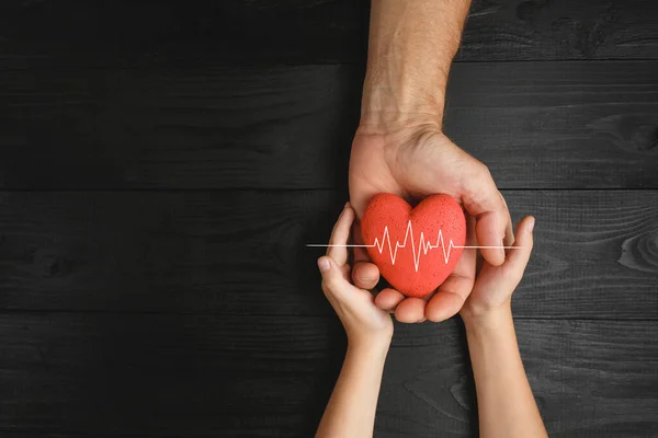 Cuore rosso in mani su sfondo scuro — Foto Stock