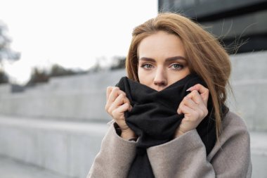 Pretty girl wraps herself in a scarf on the street