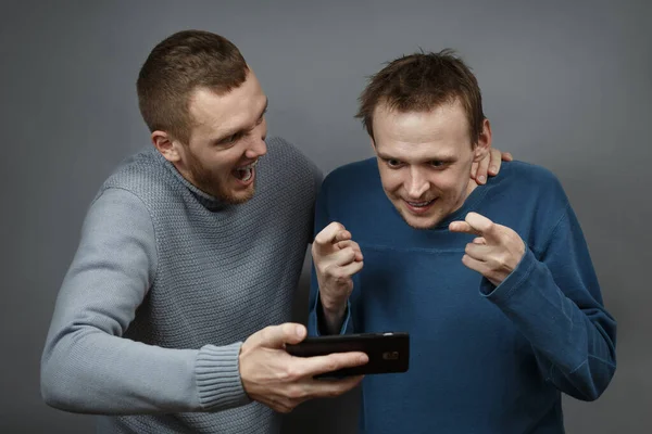Двое мужчин с возбужденным взглядом на смартфон — стоковое фото