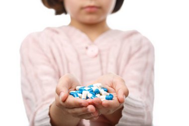 Çocuk beyaz arka planda bir avuç dolusu hap tutuyor.