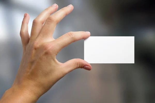 Hands holding a white business visit id card, gift, ticket, pass, present showing close up on blurred blue background. Copy space for ad text