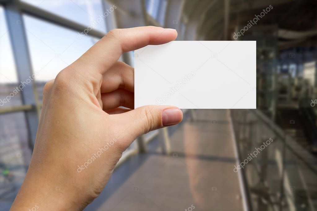 Hands holding a white business visit id card, gift, ticket, pass, present showing close up on blurred blue background. Copy space for ad text