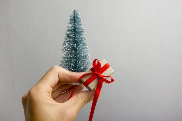 Mano femenina sosteniendo presente caja de regalo sobre fondo gris. Feliz familia celebrando el concepto de Navidad o Año Nuevo día — Foto de Stock