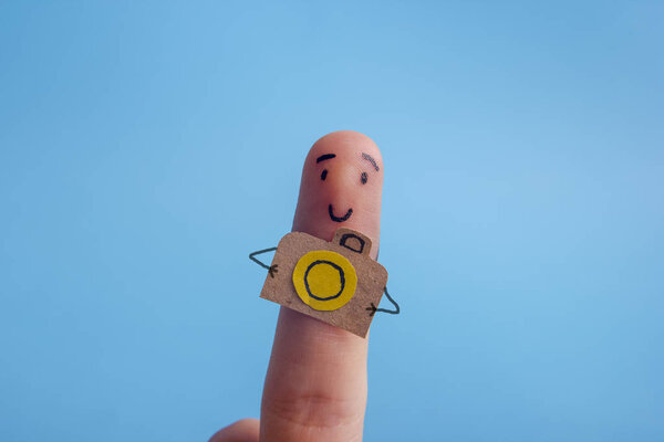 Funny finger tourist holding a camera and smiling against blue background with copy space for ad text