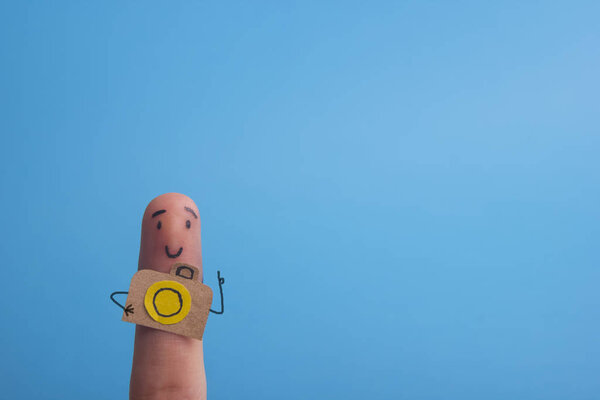 Funny finger tourist holding a camera and smiling against blue background with copy space for ad text