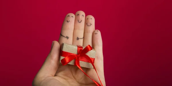 Śmieszne palce twarze prezentują pudełko na czerwonym tle z kopią miejsca na tekst. Szczęśliwa rodzina świętuje koncepcję na Boże Narodzenie lub Nowy Rok — Zdjęcie stockowe