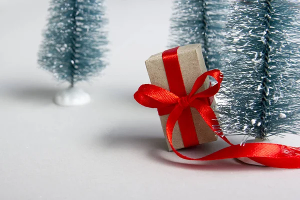 Caja regalo regalo de Navidad con cinta roja sobre fondo blanco y árbol de Navidad. Copia espacio para texto. Enfoque selectivo . — Foto de Stock