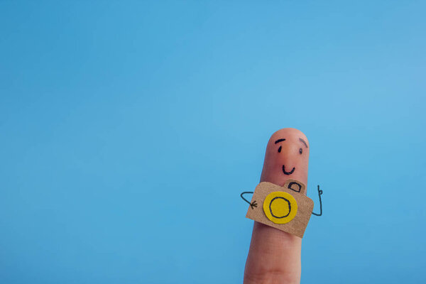 Funny finger tourist holding a camera and smiling against blue background with copy space for ad text