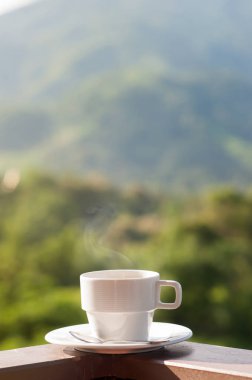 Beyaz fincan sıcak kahve ile doğal ve dağların balkonunda.