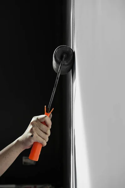 Mão segurando pintura rolo aplicando tinta cinza na parede branca . — Fotografia de Stock
