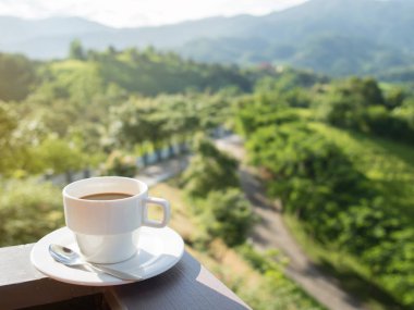 Beyaz fincan sıcak kahve ile doğal ve dağların balkonunda.