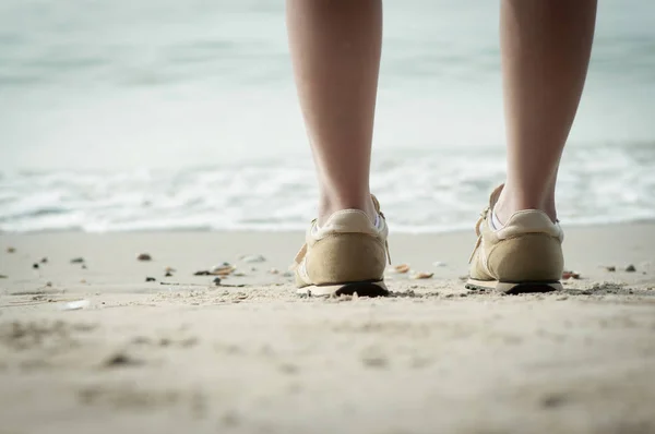 Pierna de mujer de pie en la playa de arena en el mar . — Foto de Stock