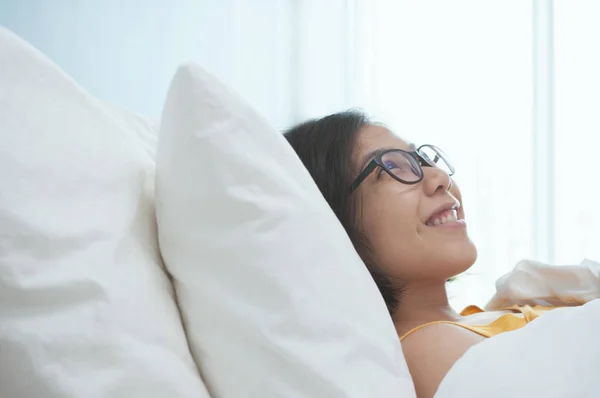 Счастье молодых азиатских очков женщина улыбается и лежит на кровати — стоковое фото