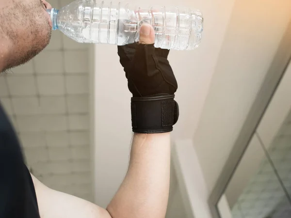 man hands wear gloves holding bottle of water at a gym.