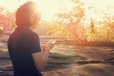 Asyalı kız doğa arka plan ile Smartphone kullanarak. 