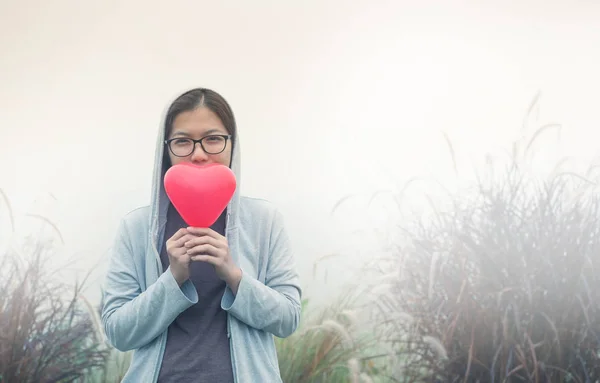 Asiática mujer sosteniendo rojo corazón en flor hierba campo . — Foto de Stock