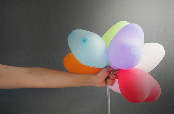 Mulher mão segurando balões multicoloridos forma do coração em cinza backg — Fotografia de Stock