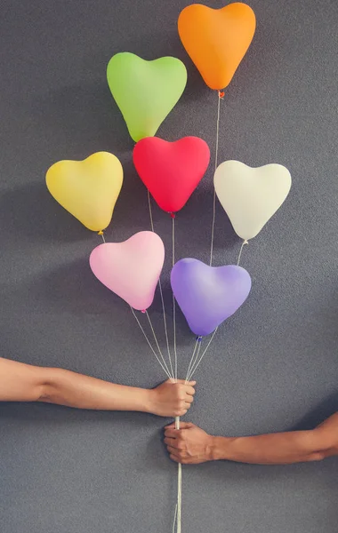 Pareja manos sosteniendo globos multicolor forma de corazón en bac gris — Foto de Stock