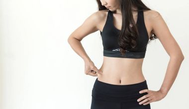 Genç Asyalı kadın karnı beyaz izole arka plan üzerinde sıkışmak.