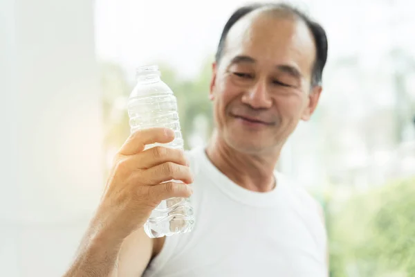 Close up Asian senior man holding bottle of water at a gym.