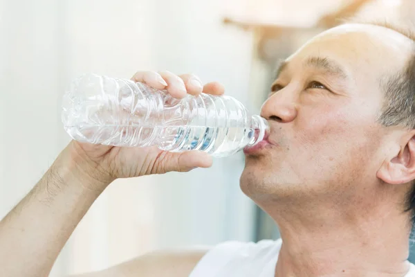 Asian senior man drinking water at a gym. Tired, thirstily.