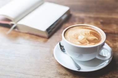 Bir fincan kahve ile ahşap masa üstünde açık defter.