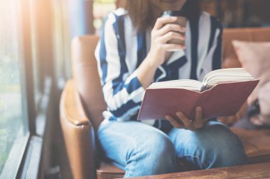 Kitap üzerinde odaklanın. Bir fincan kahve ve r tutan Asyalı kadın rahat