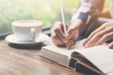 Closeup kadın defter üzerinde kalemle yazma. Bir fincan kahve o
