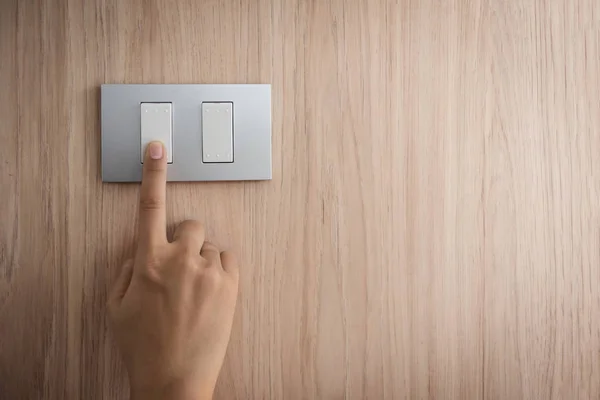 Fermer main allumée ou éteinte sur interrupteur lumineux gris avec bois — Photo