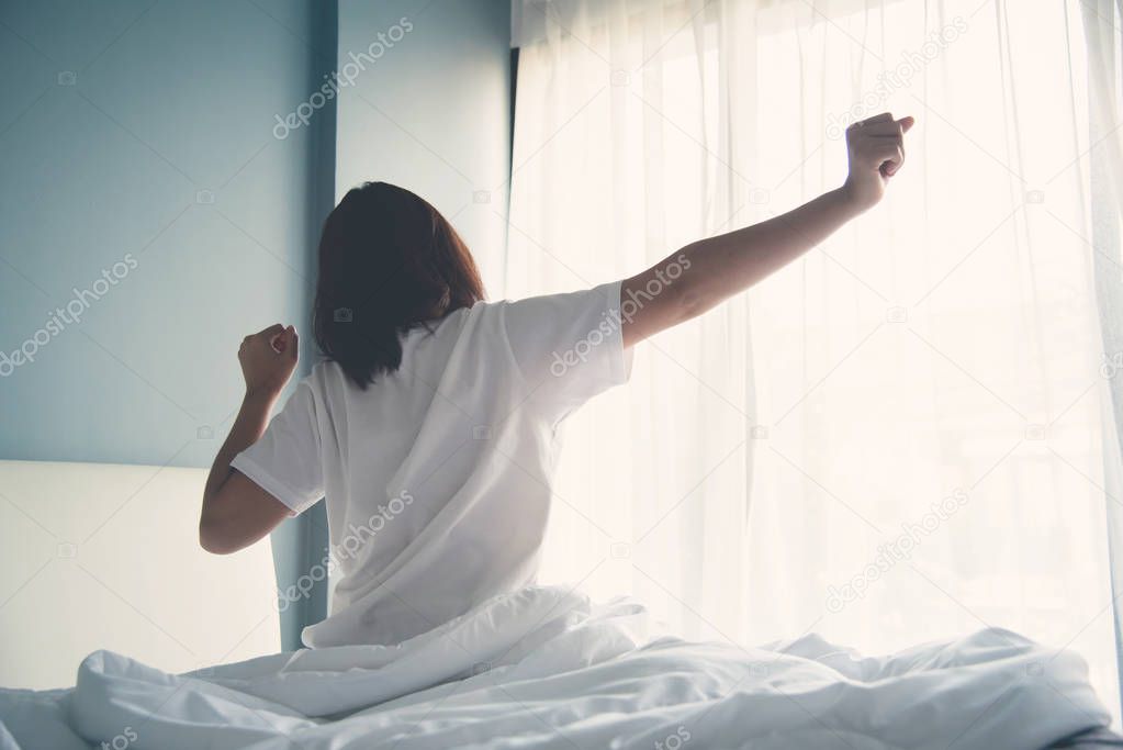 Asian woman waking up in the morning. Outstretched arms.