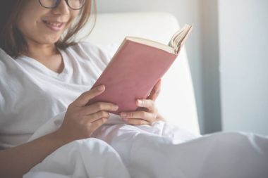 Asya gözlük kadın onun yatağında bir kitap okuma.