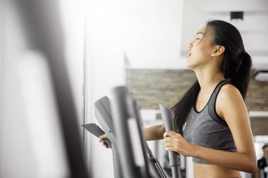 Asyalı kadın spor salonunda eliptik eğitmen makinede egzersiz.
