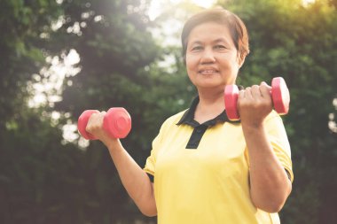 Asya kıdemli kadın doğal arka plan üzerinde halter kaldırma.