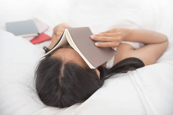 Uvolněné asijské dívka spí na posteli s knihou na její tváři. — Stock fotografie