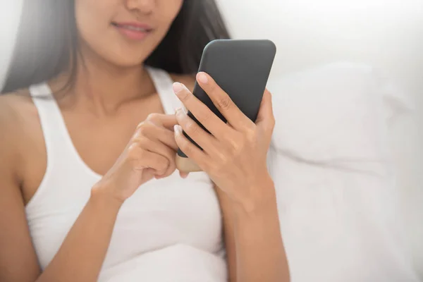 Nahaufnahme einer Frau mit Smartphone auf ihrem Bett. — Stockfoto