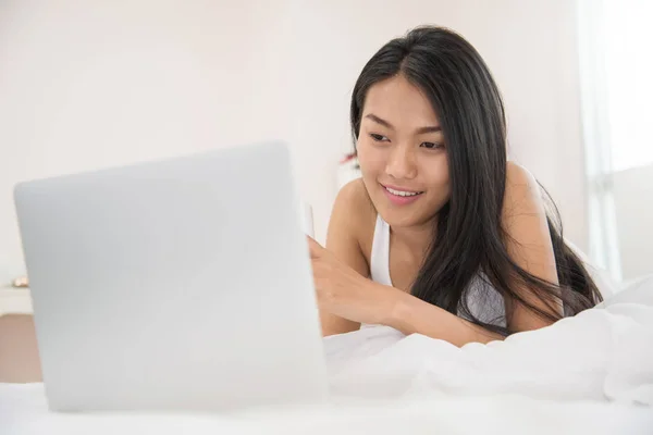 Bonheur asiatique fille souriant et en utilisant sur ordinateur portable sur son lit . — Photo