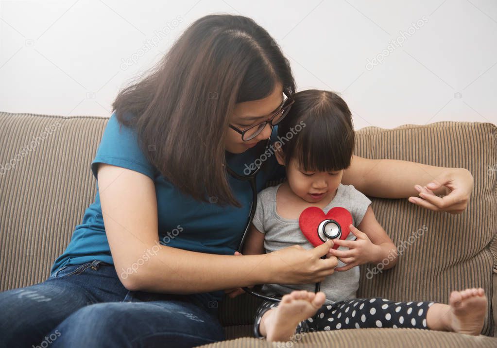 Asian young mother examining heartbeat of little kid girl