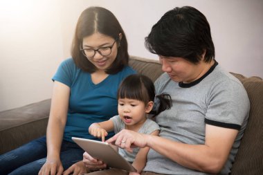 Mutluluğu ile oturan ve dijital tablet oynarken Asya ailesi.