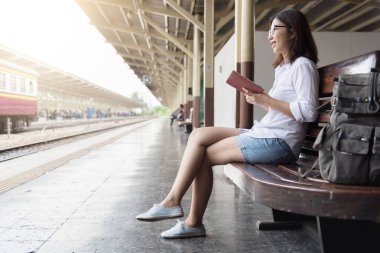 Asyalı kadın backpacker tren istasyonunda oturuyor.