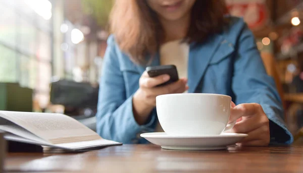Жінка руки тримає чашку кави і використовує смартфон . — стокове фото