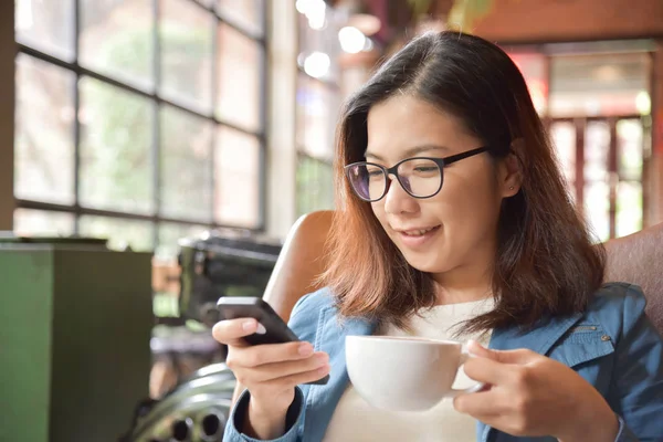 Жінка тримає чашку кави і використовує смартфон . — стокове фото