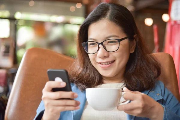 Женщина держит чашку кофе и с помощью смартфона . — стоковое фото