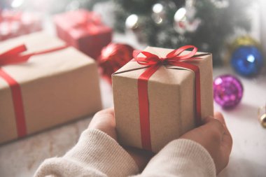 Kahverengi bir hediye kutusu tutan eller.